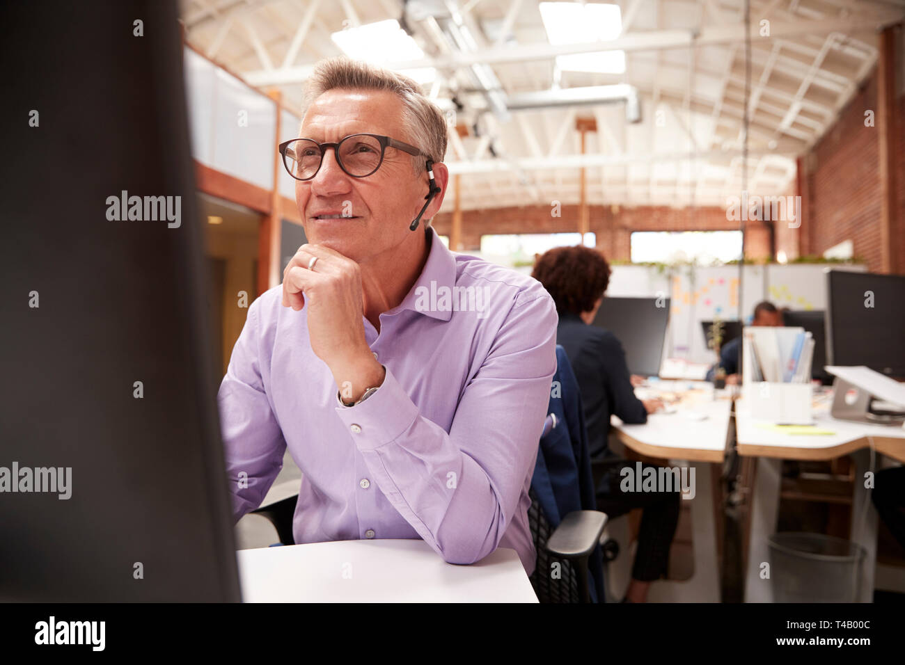 Mature Male Customer Services Agent Working At Desk In Call Center Stock Photo