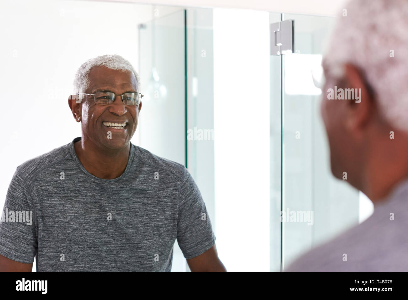 Smiling Senior Man Looking At Reflection In Bathroom Mirror Wearing Pajamas Stock Photo