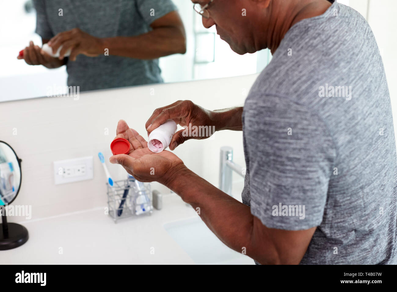 Close Up Of Senior Man In Bathroom Mirror Wearing Pajamas Holding Vitamin Supplement Tablets Stock Photo