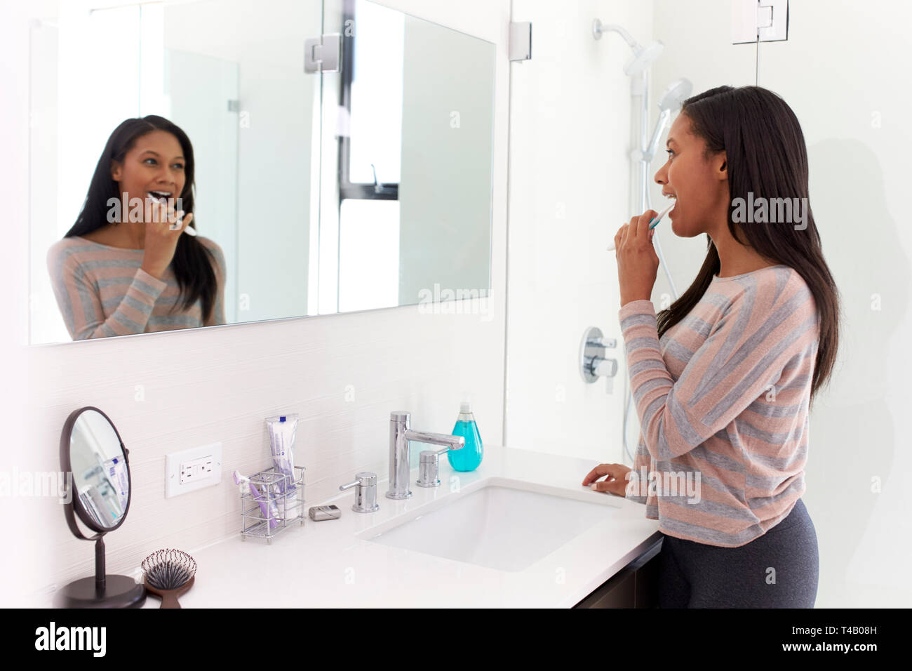 Woman Looking At Reflection In Bathroom Mirror Brushing Teeth Stock Photo