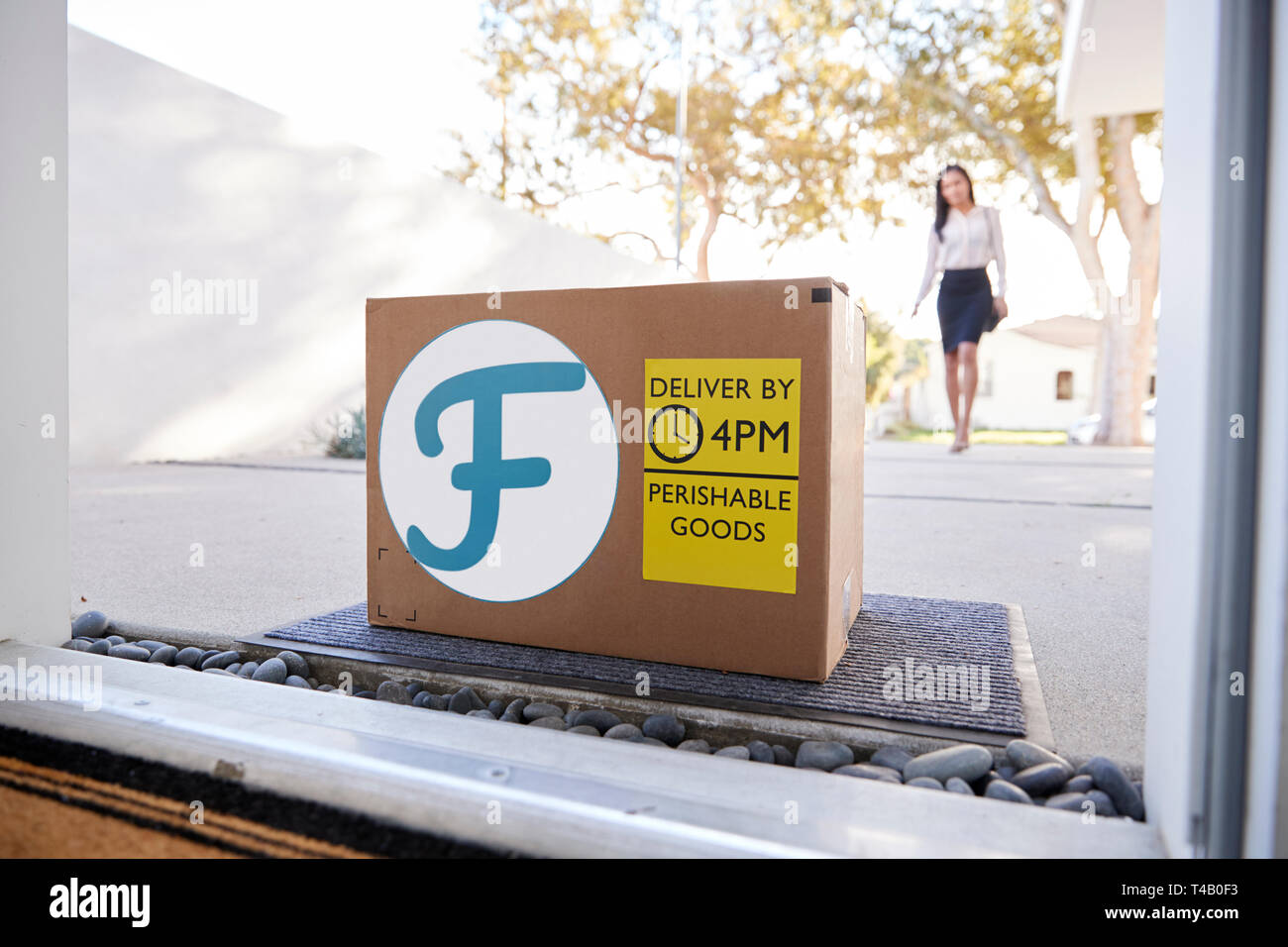 Businesswoman Coming Home To Fresh Food Home Delivery In Cardboard Box Outside Front Door Stock Photo