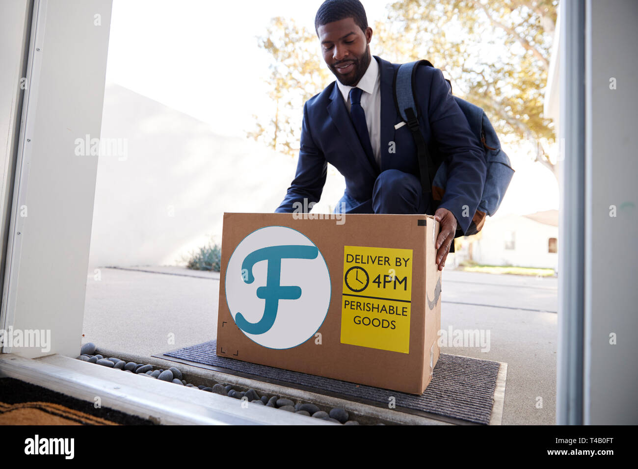 Businessman Coming Home To Fresh Food Home Delivery In Cardboard Box Outside Front Door Stock Photo