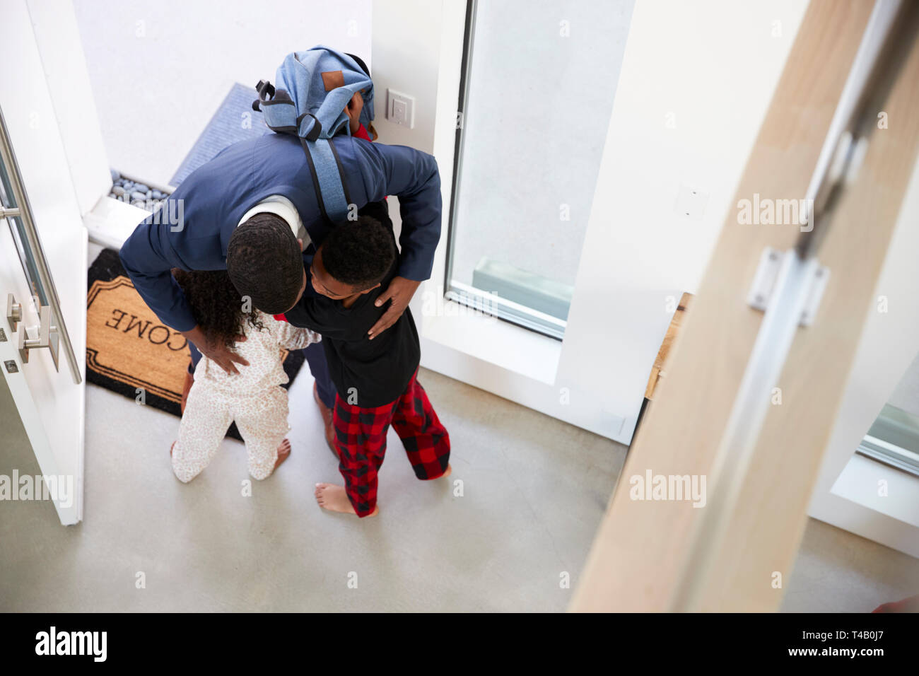 Children Greeting And Hugging Working Businessman Mother As She Returns Home From Work Stock Photo