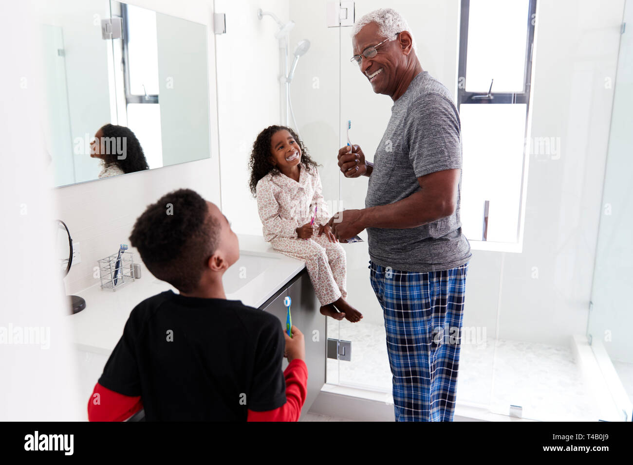 Grandfather In Bathroom Wearing Pajamas Brushing Teeth With Grandchildren Stock Photo