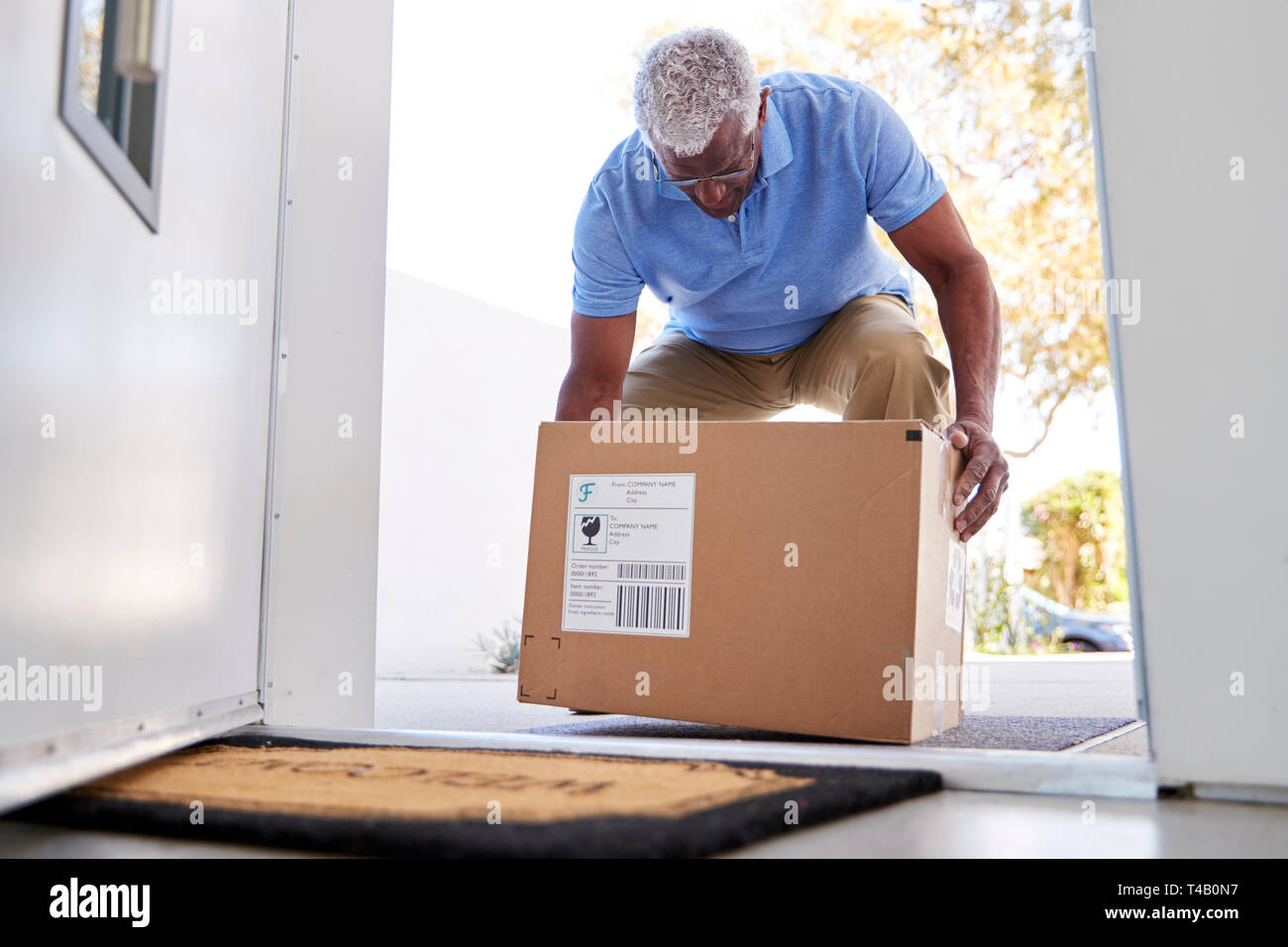 Senior Man Coming Back To Home Delivery In Cardboard Box Outside Front Door Stock Photo