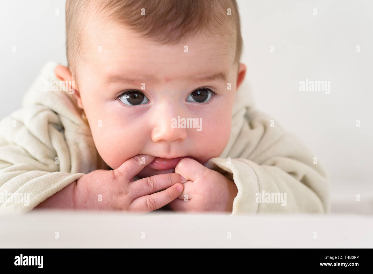 Portrait of an adorable smiling baby biting her own fingers putting her