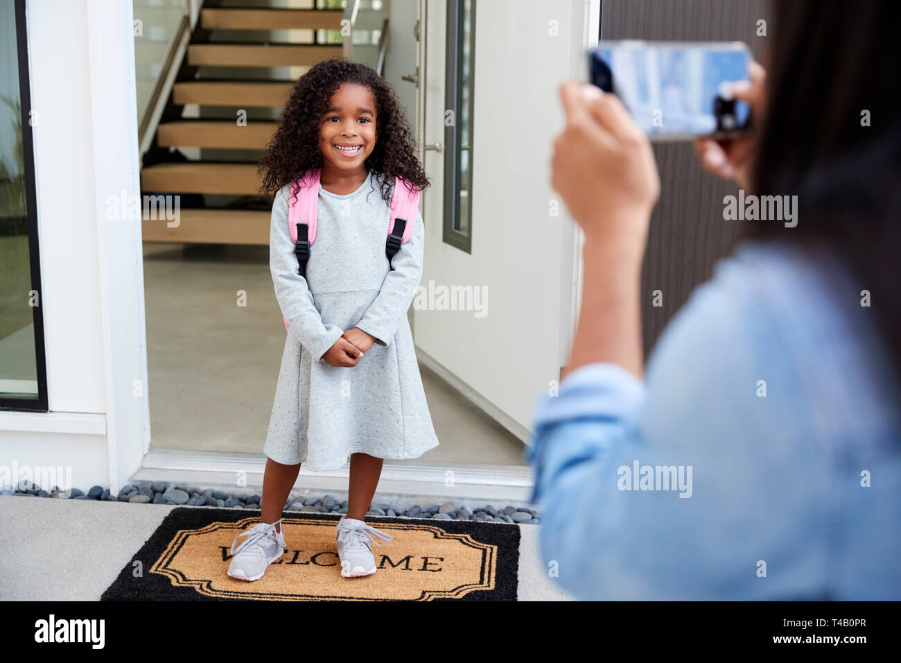 Mother Taking Photo Of Daughter With Cell Phone On First Day Back At School Stock Photo