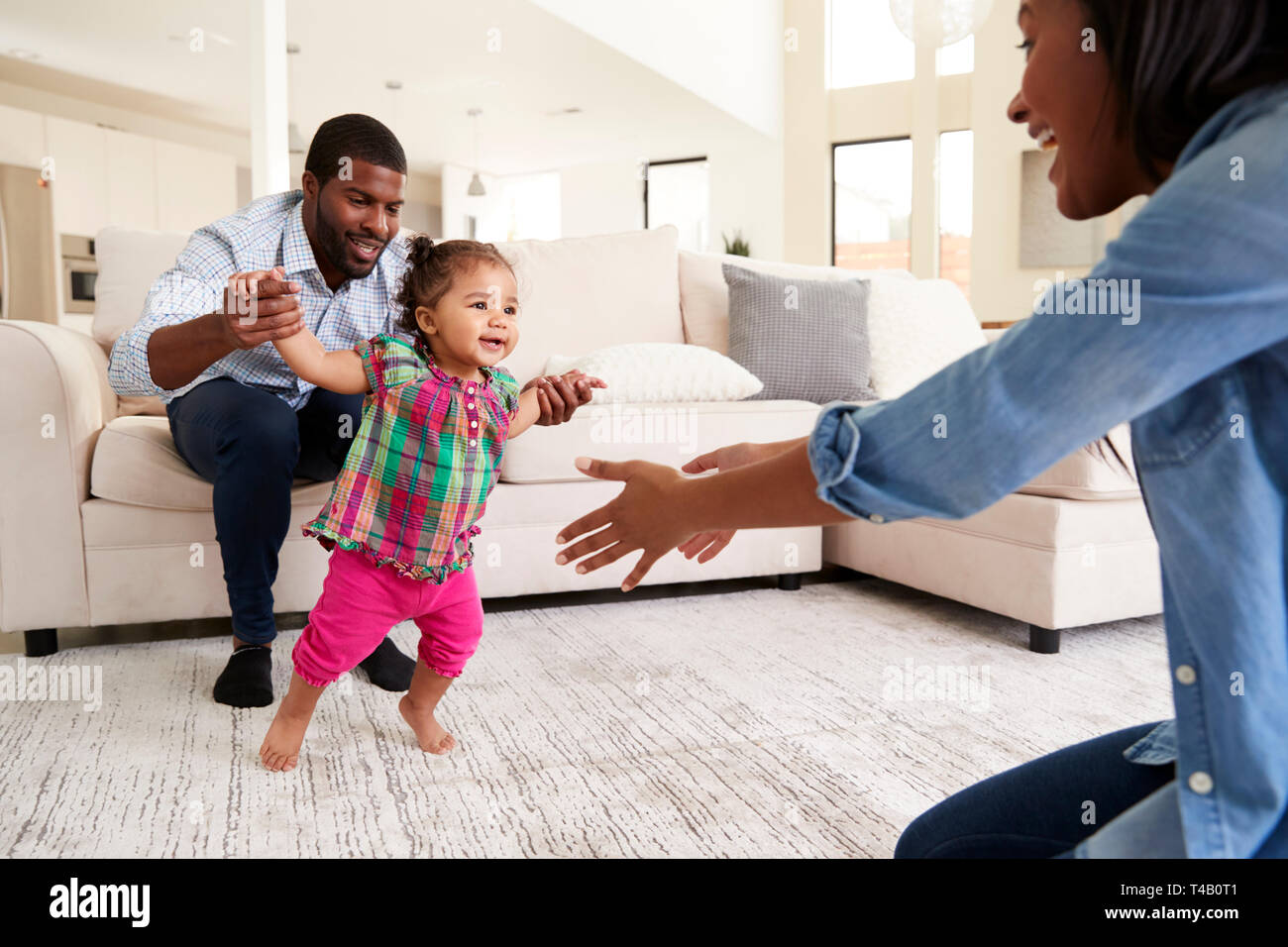 Family At Home Encouraging Baby Daughter To Take First Steps Stock Photo