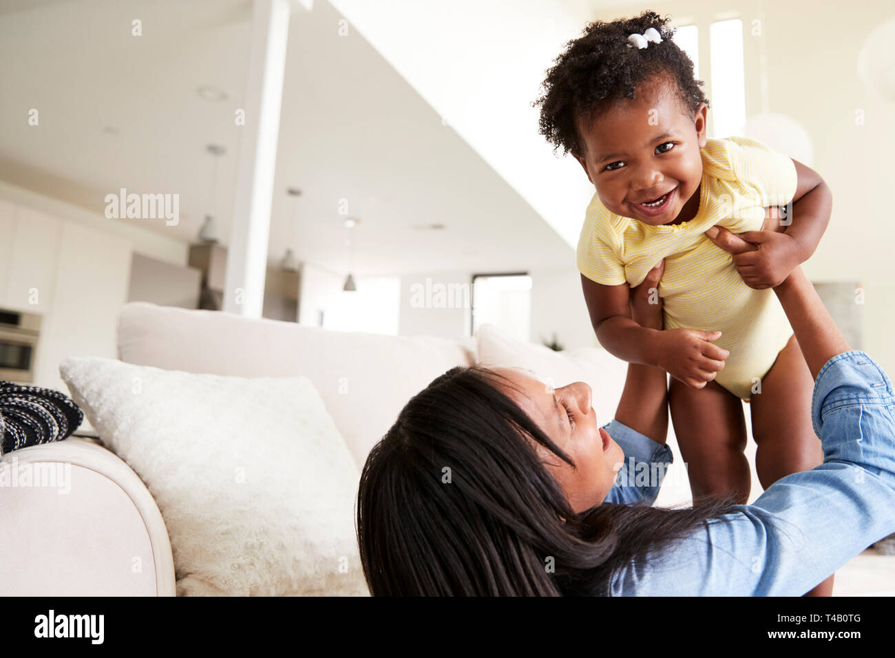 Mother Playing With Baby Daughter Lifting Her In The Air At Home Stock Photo