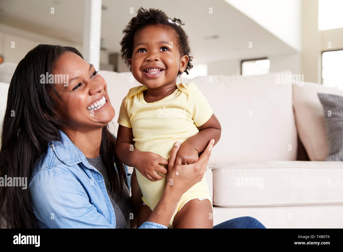 Mother Playing With Baby Daughter Sitting On Floor Of Lounge At Home Stock Photo