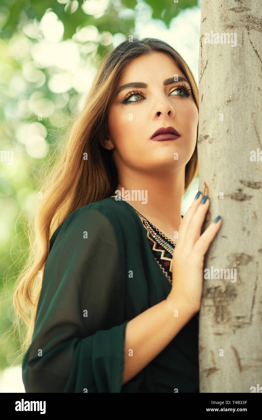 Beautiful young woman leaning against tree looking away Stock Photo