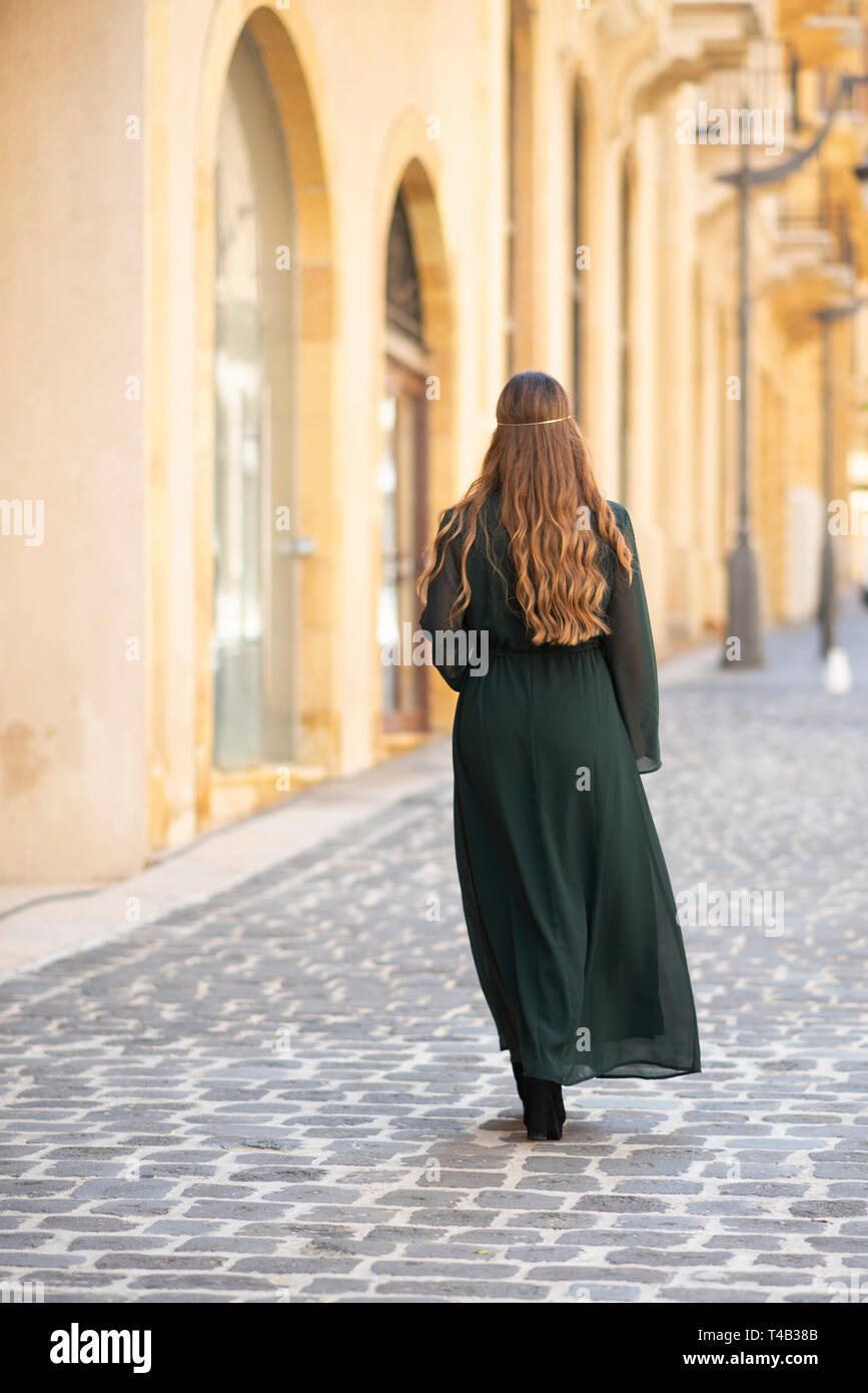 Rear view of woman walking away on cobbled road Stock Photo