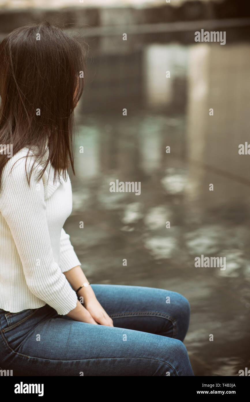 Young woman sitting alone outdoors looking away Stock Photo