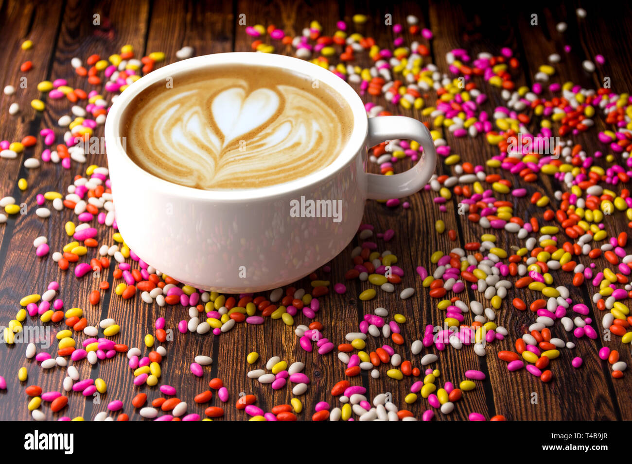 Cup of Cappuccino coffee on a wooden table with colorful sweet candies fresh and healthy tea Stock Photo