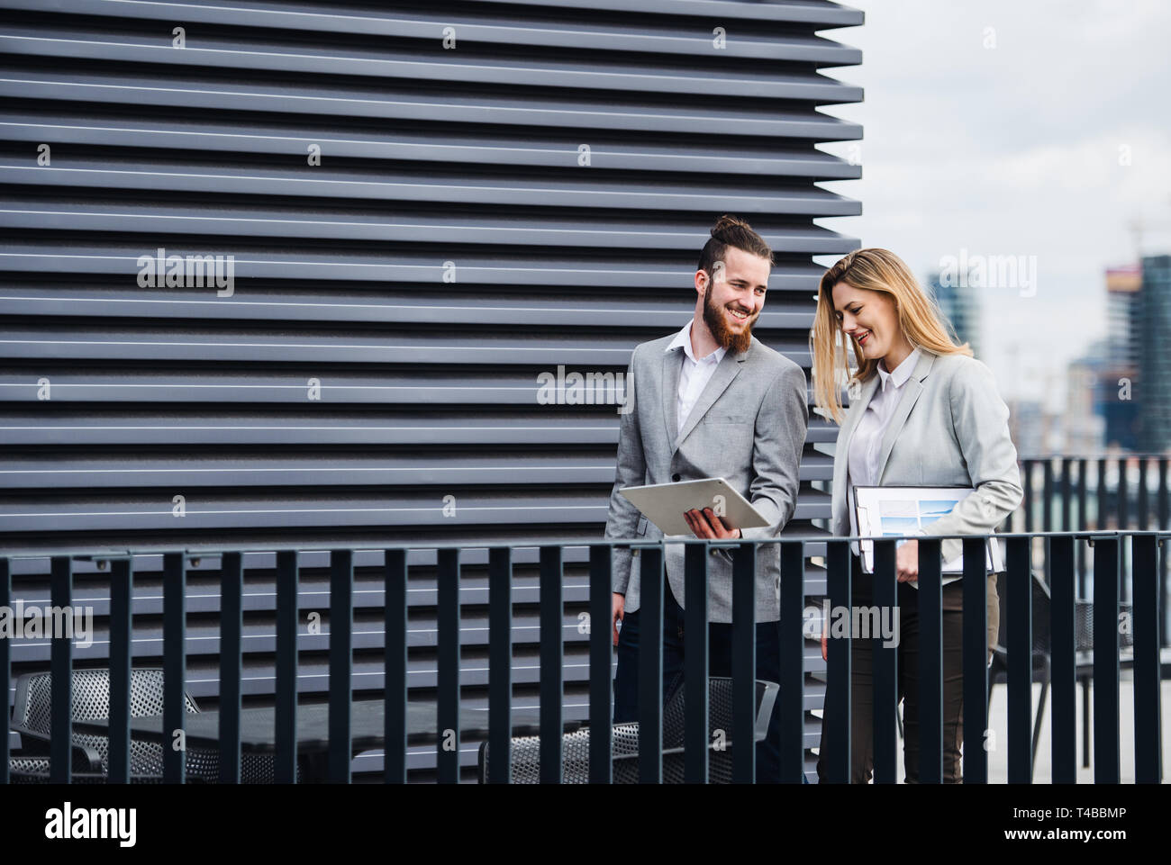 Two young business people with tablet standing on a terrace outside office, working. Stock Photo