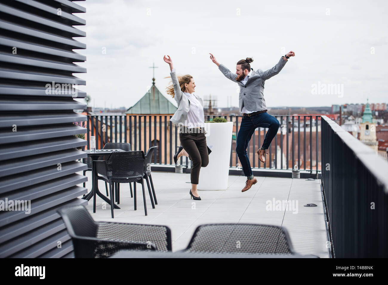 Two young business people jumping on terrace outside office, expressing excitement. Stock Photo