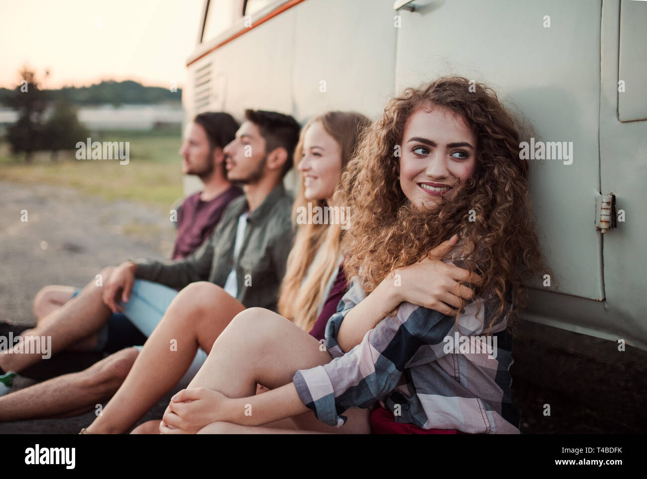 A group of young friends on a roadtrip through countryside, sitting by a minivan. Stock Photo