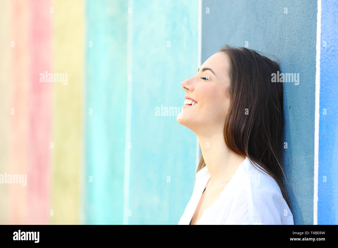 Side view portrait of a happy woman resting leaning on a colorful wall in the street Stock Photo