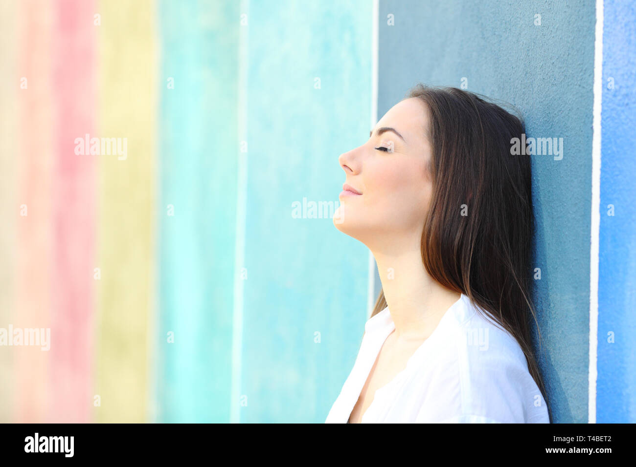 Side view portrait of a relaxed woman resting leaning on a colorful wall in the street Stock Photo