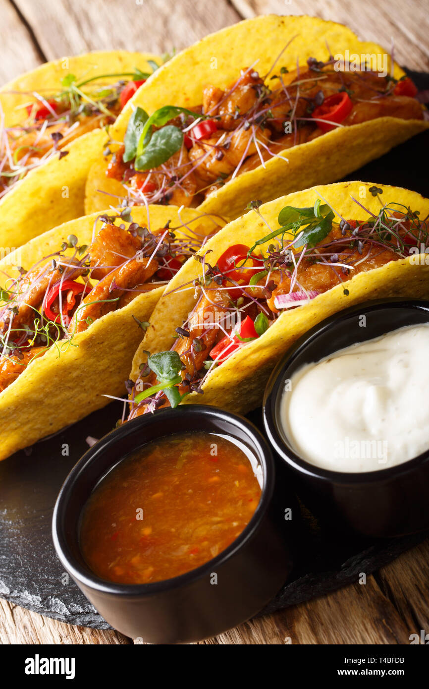 Mexican tacos stuffed  with glazed chicken, microgreen and vegetables close-up on the table. vertical Stock Photo