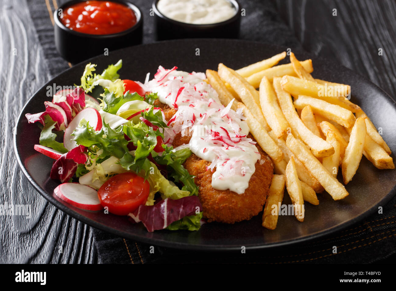 Served fried pollock in breading with french fries and fresh salad close-up on a plate and sauces on the table. horizontal Stock Photo