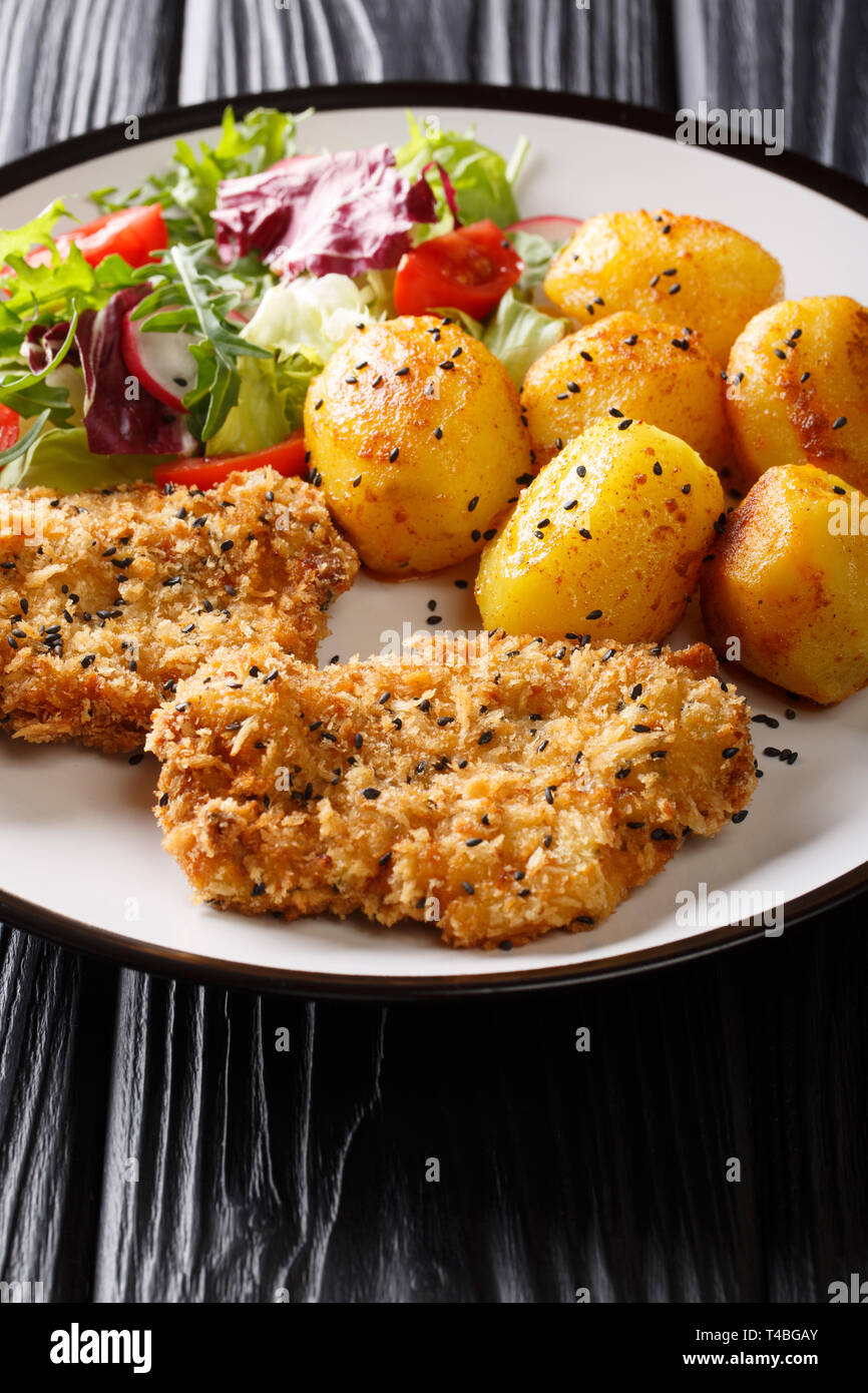 Pork cutlet in sesame breading with new potatoes and fresh salad close-up on a plate on the table. vertical Stock Photo