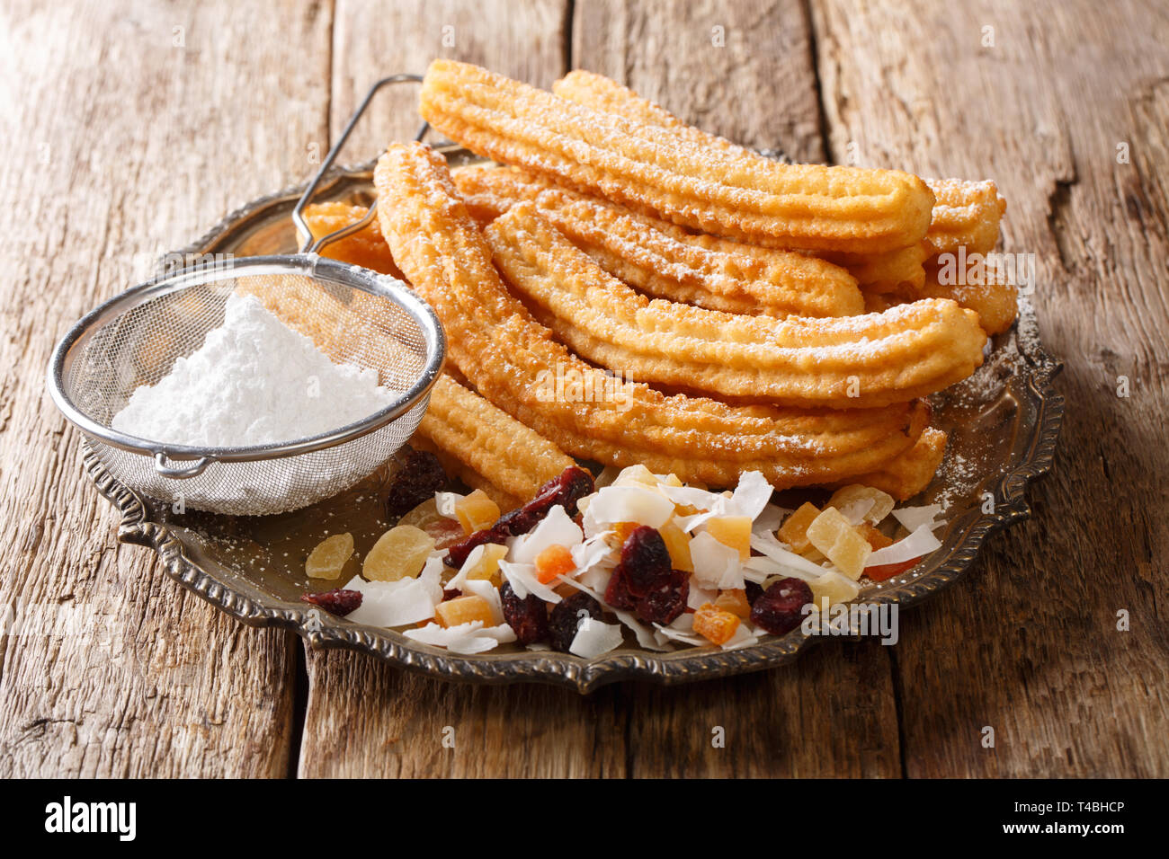 Churros are a fried pastry that are rolled in sugar and served with a candied fruit close-up on a plate on the table. horizontal Stock Photo