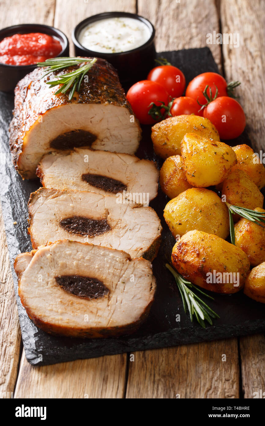 Baked pork roll stuffed with prunes served with new potatoes and sauces close-up on the table. vertical Stock Photo