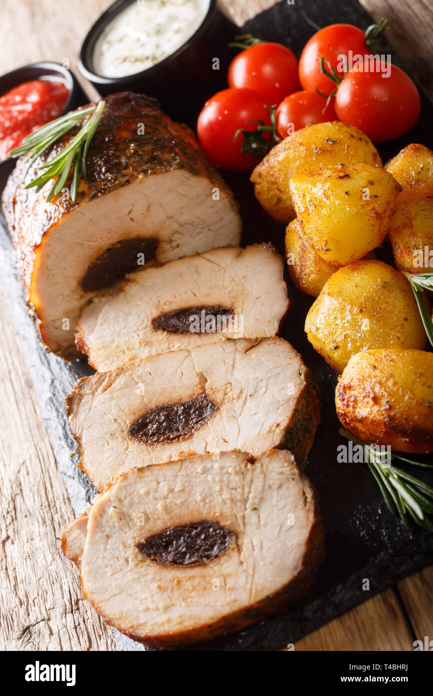 Baked pork with prunes served with young potatoes and sauces close-up on the table. vertical Stock Photo