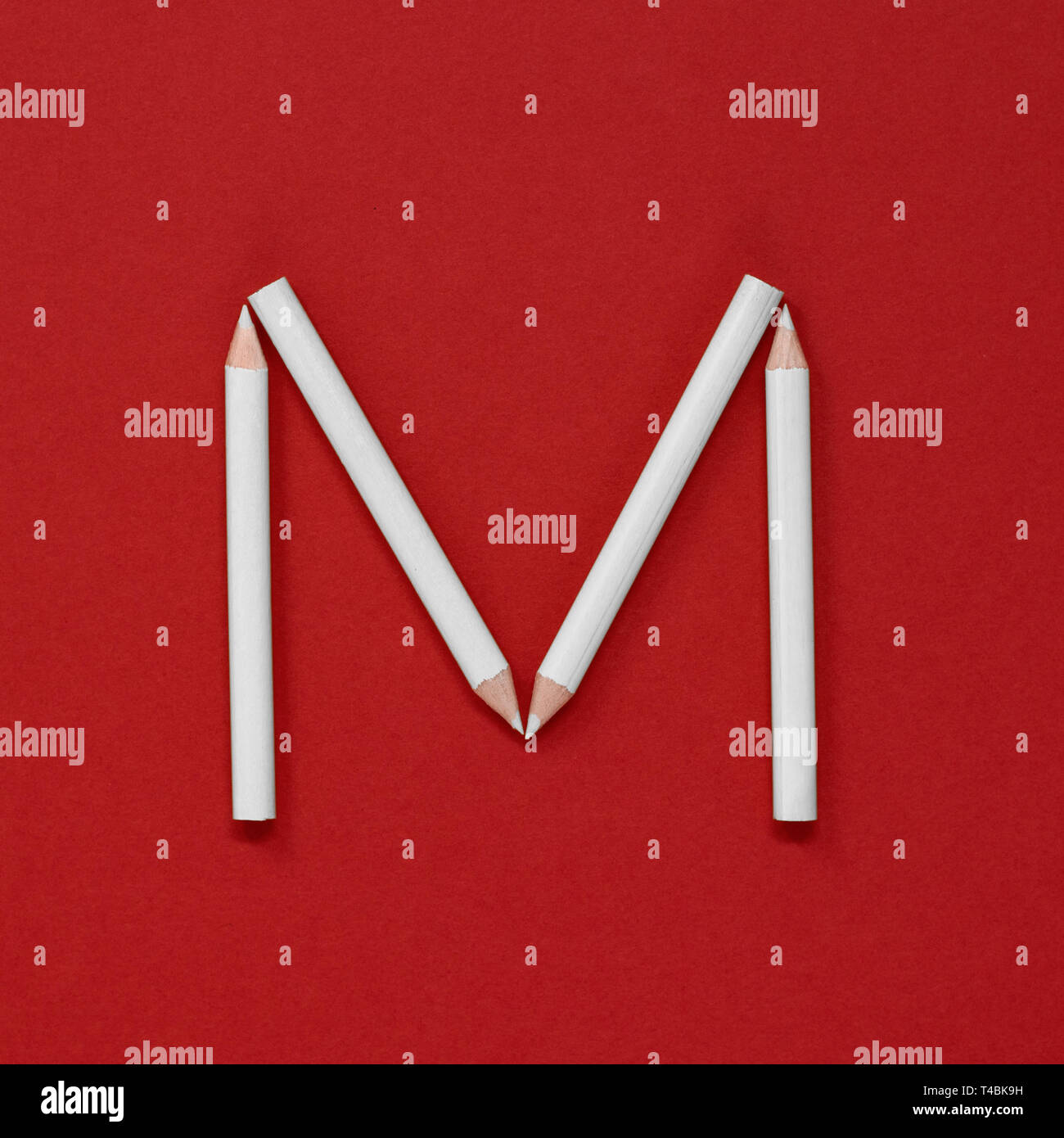 The letter 'M' made from grad-white pencils on a plain red background Stock Photo