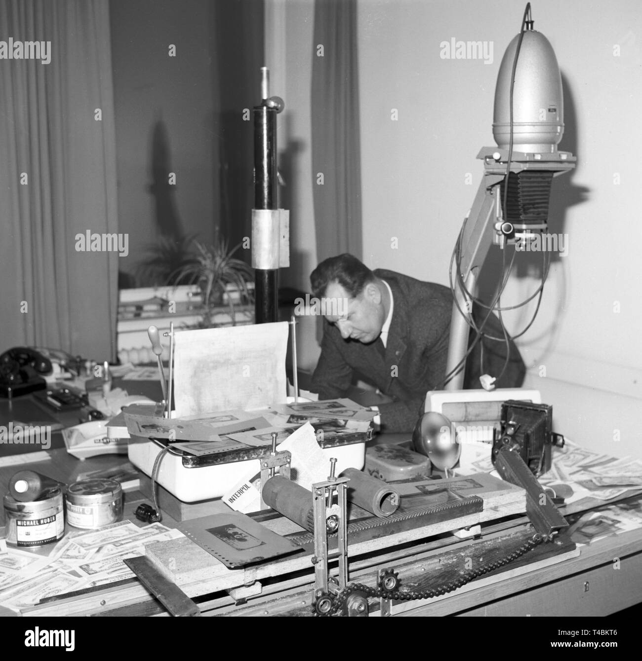 The criminal investigation department of Nuremberg has revealed a counterfeiter workshop. The picture shows an officer leaning over the counterfeiter's desk on 13 December 1963. | usage worldwide Stock Photo