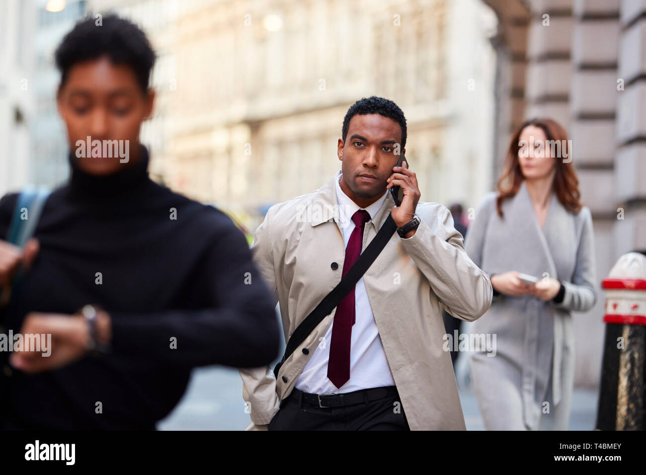 Millennial black businessman walking in a busy London street using smartphone, selective focus Stock Photo