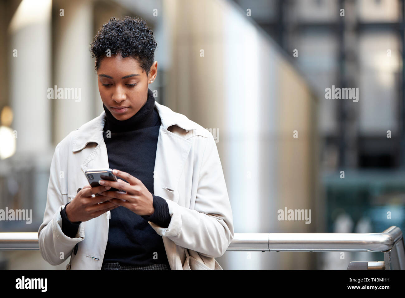 Young adult woman standing in a business area of the city using her smartphone, focus on foreground Stock Photo