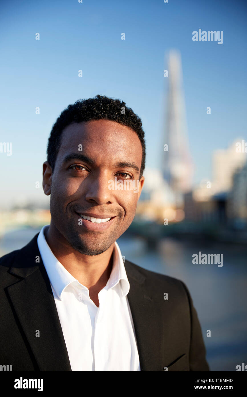 Young black businessman in smart casual clothing standing by the River Thames in London smiling to camera, close up Stock Photo