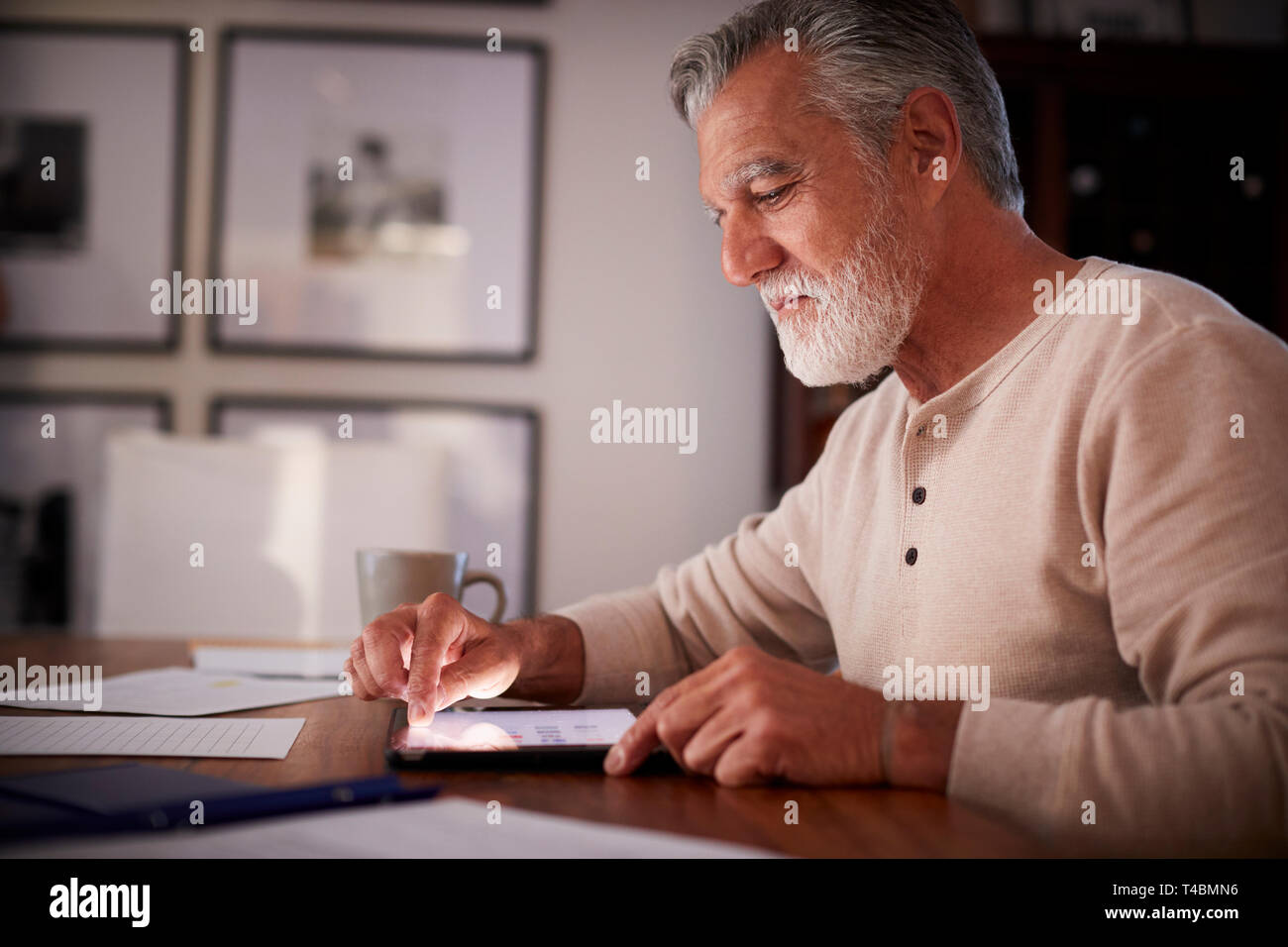 Senior Hispanic man sitting at a table using a tablet computer  in the evening, close up, side view Stock Photo