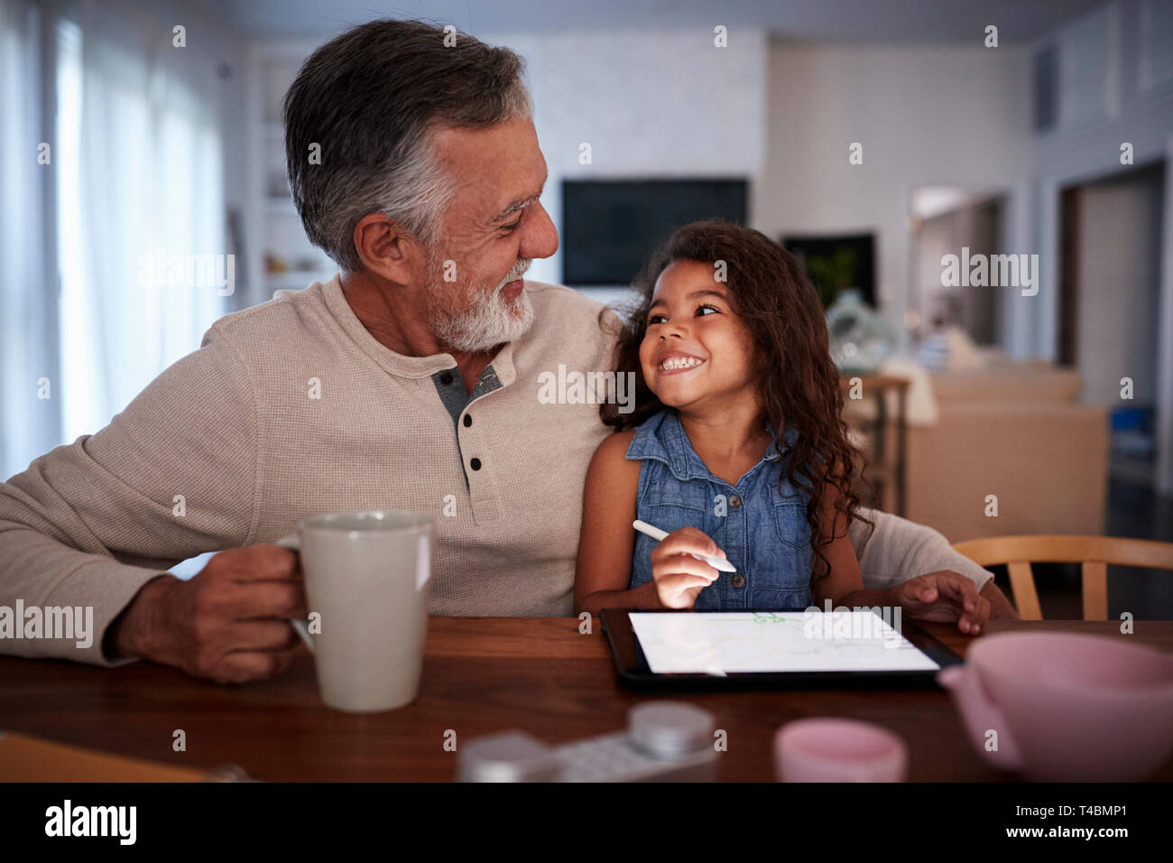 Senior Hispanic man with his granddaughter using tablet computer, looking at each other, front view Stock Photo
