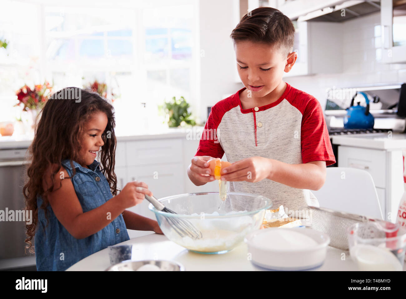 Brother and sister preparing cake mixture together at the kitchen table, waist up Stock Photo