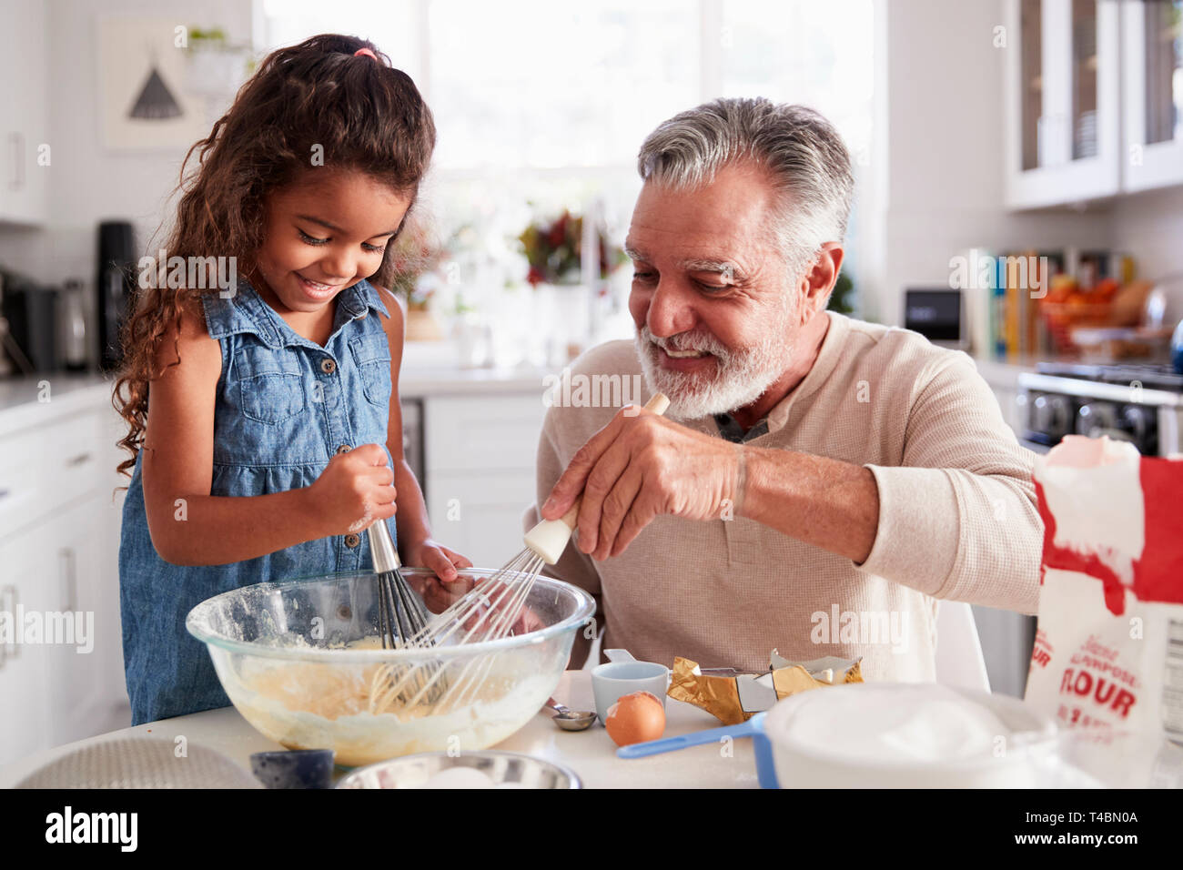 Young Hispanic girl and her grandad whisking cake mixture together at the kitchen table, close up Stock Photo