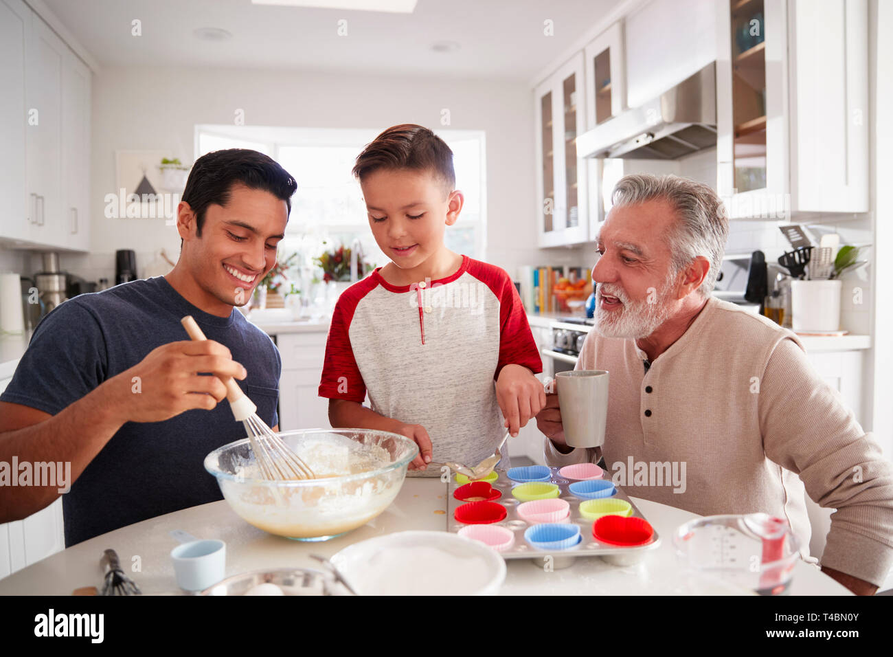 Three male generations of family preparing cakes together at the table in the kitchen, close up Stock Photo