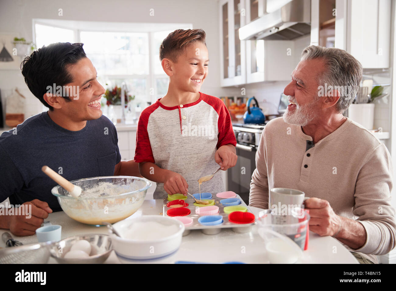 Three male generations of family making cakes together at the table in ...