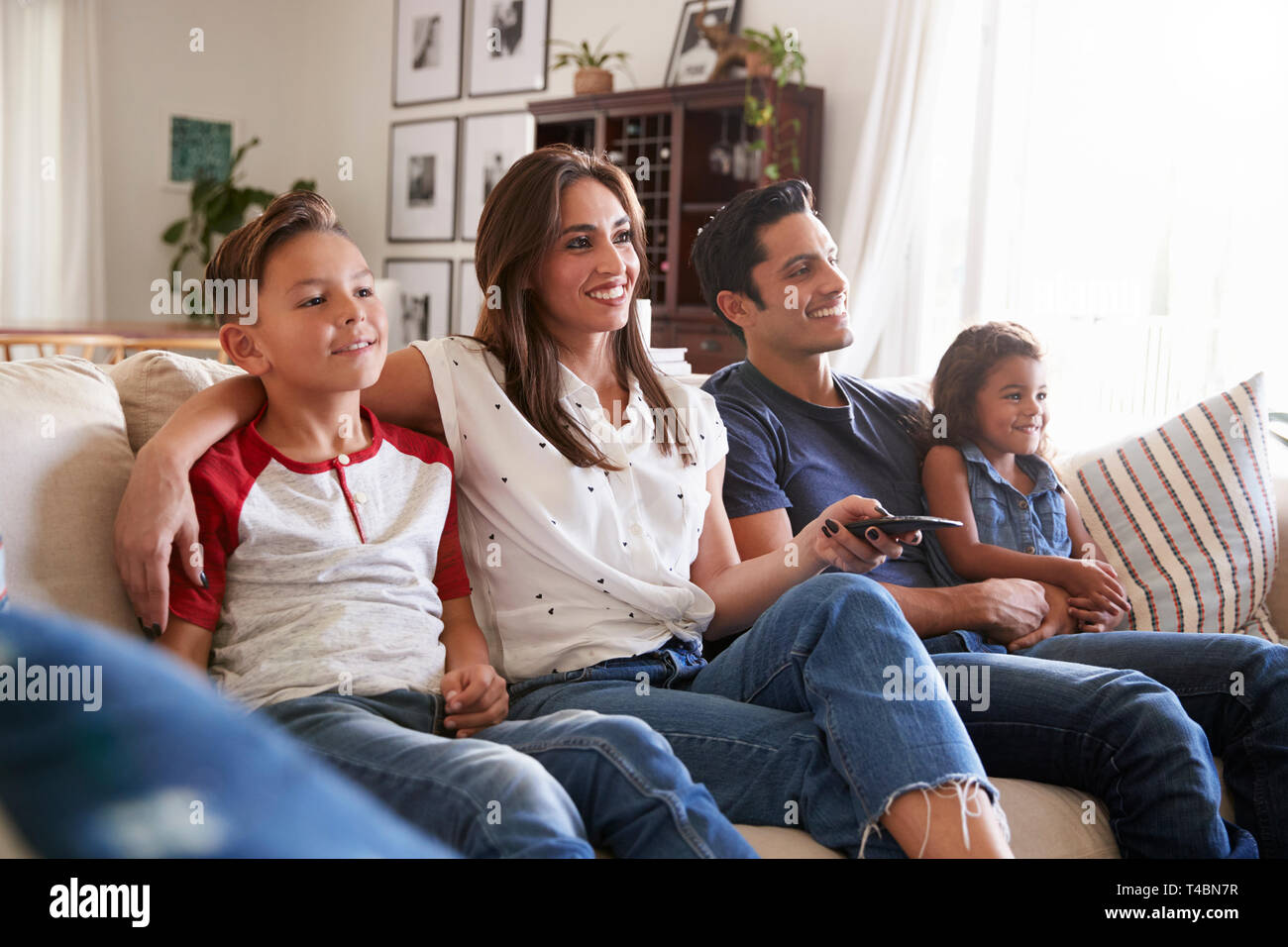 Young Hispanic family sitting on the sofa at home watching TV togther, close up Stock Photo