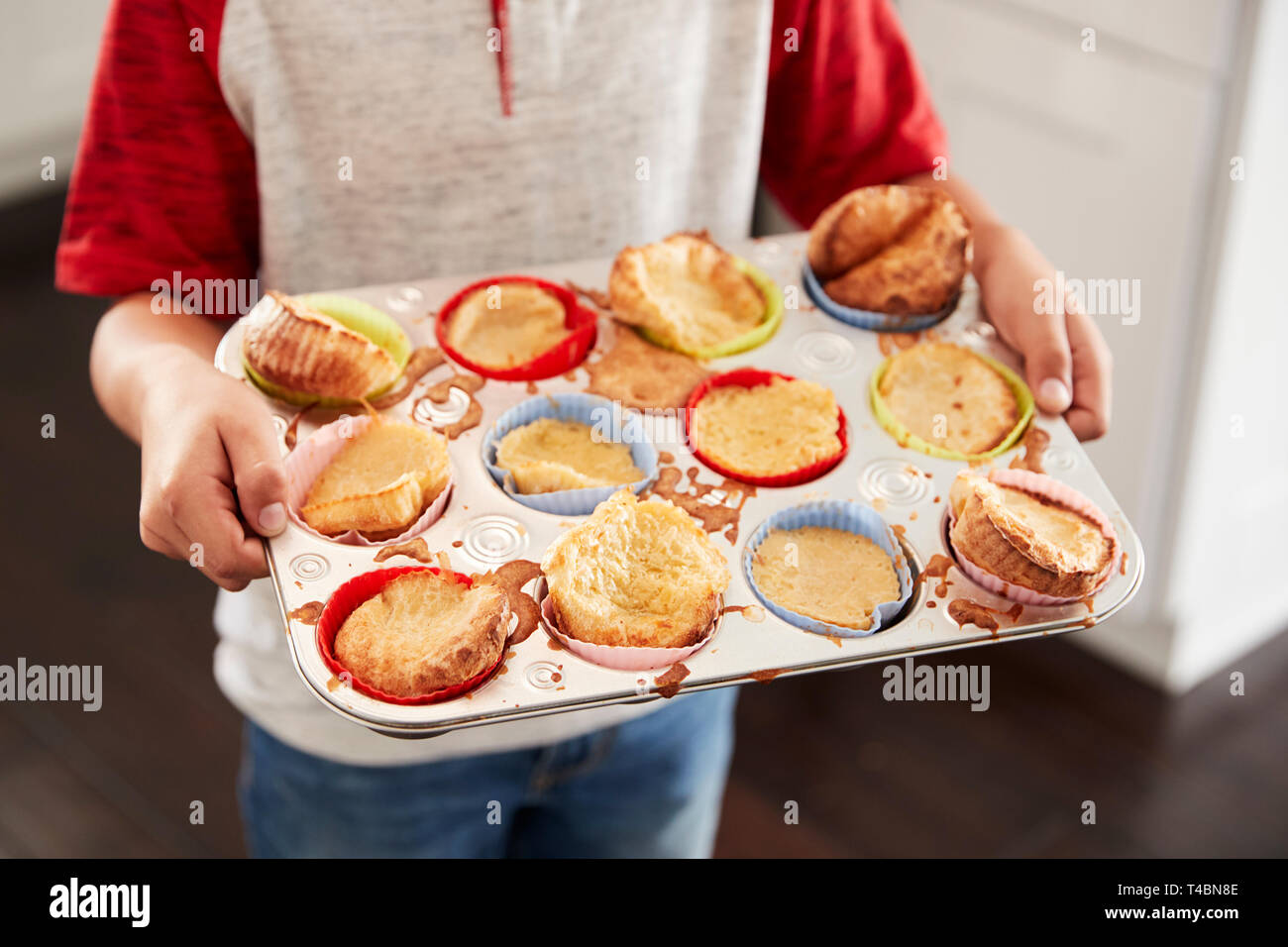 Boy holding baking tray, presenting the cakes he has baked to camera, mid section, close up Stock Photo
