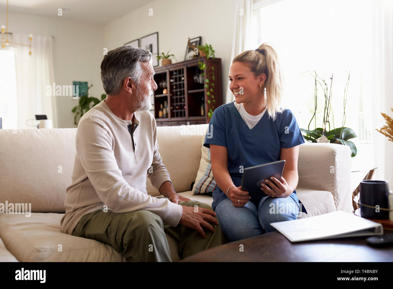 Female healthcare worker using a tablet computer with a senior Hispanic man during a home visit Stock Photo
