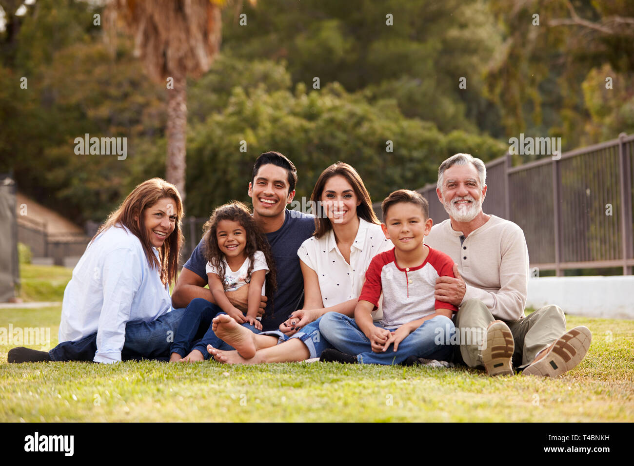 Three generation Hispanic family sitting on the grass in the park smiling to camera, selective focus Stock Photo