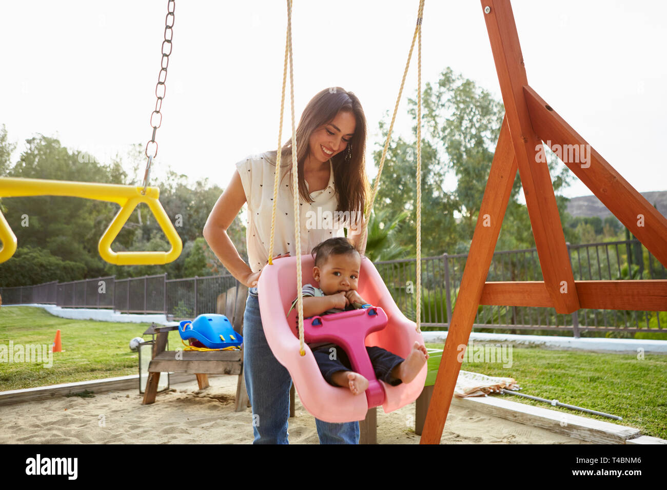Young Hispanic Mother Pushing Her Baby On A Swing At A