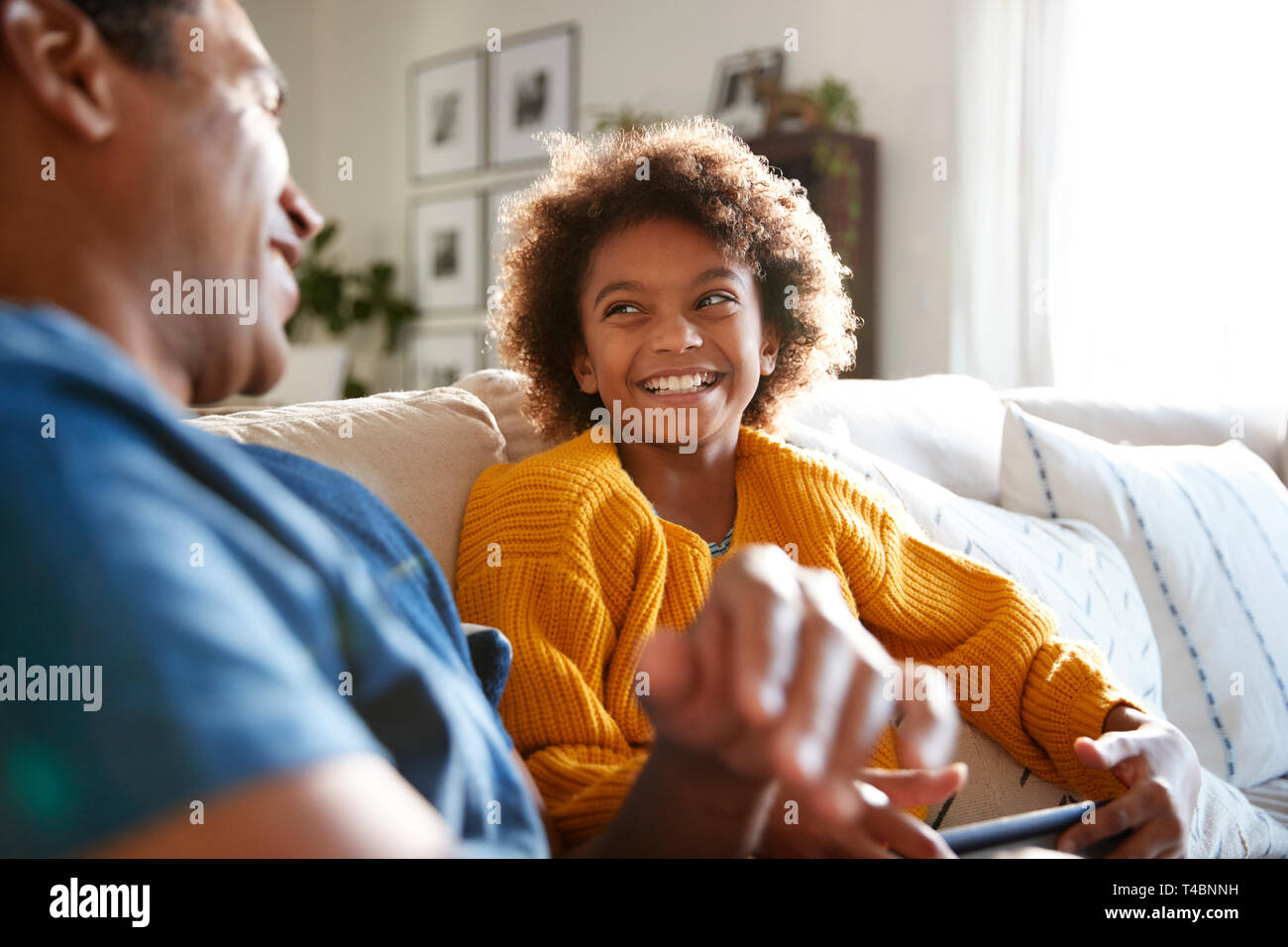Close up of father and daughter sitting on sofa in the living room looking at each other and laughing, selective focus Stock Photo