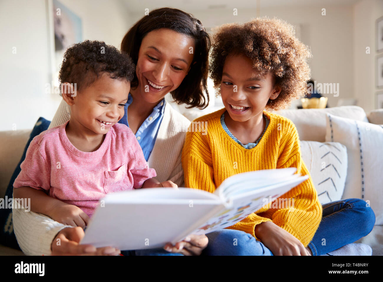 Close up of young mother sitting on sofa in the living room with her children, reading them a book, low angle Stock Photo