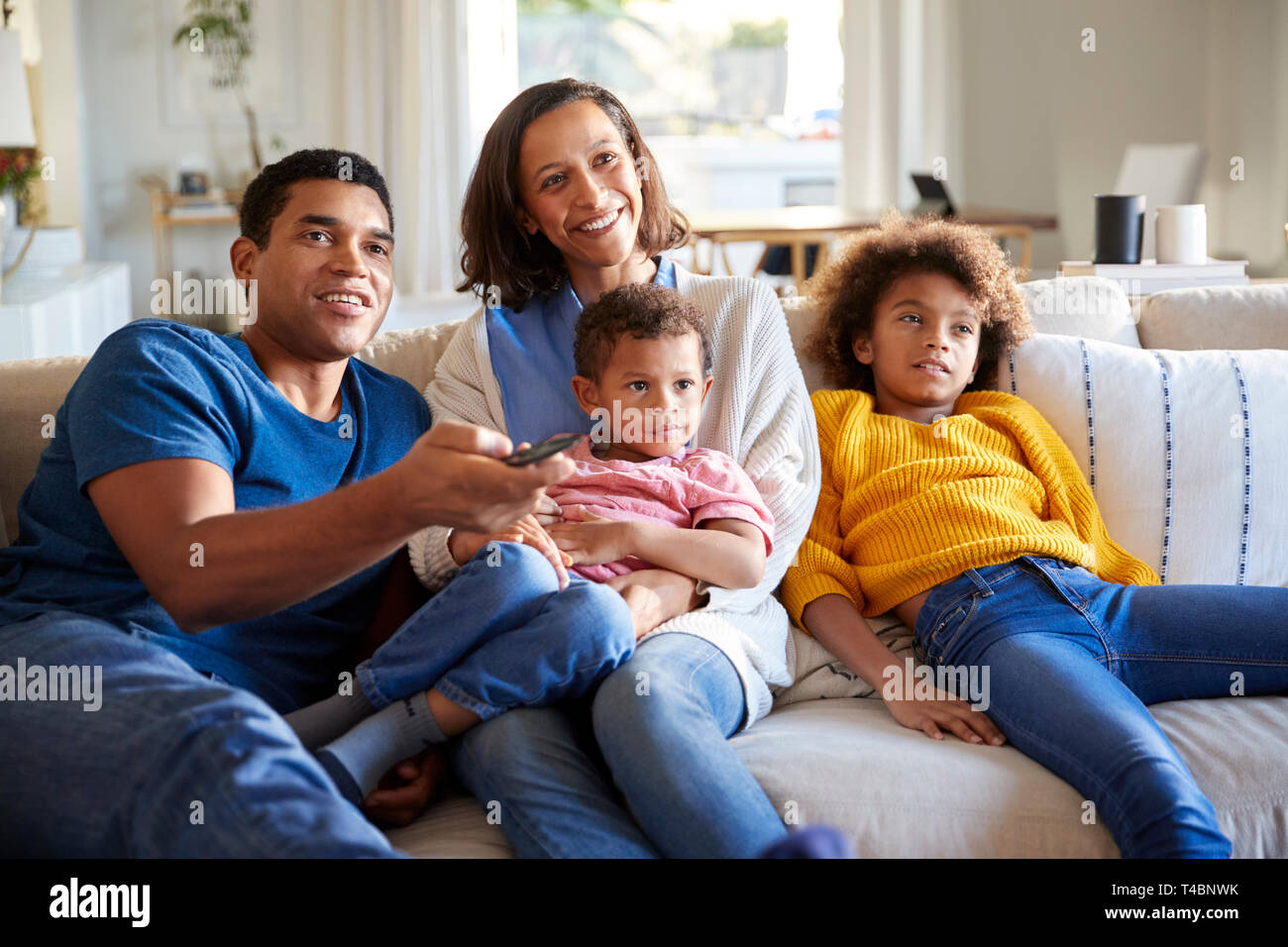 Front view of young family sitting together on the sofa in their living room watching TV, close up, front view Stock Photo