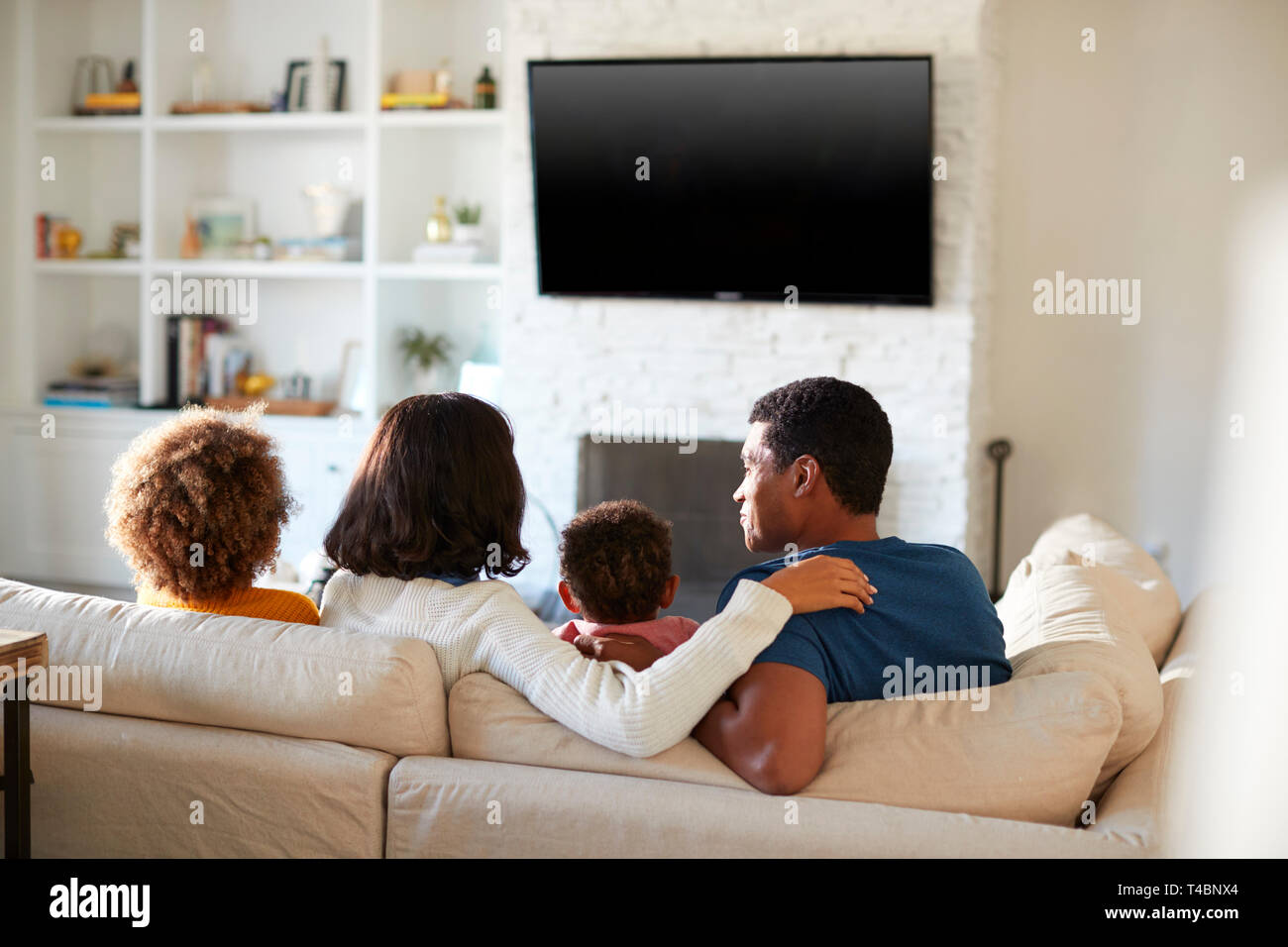 Back view of young family sitting on the sofa and watching TV together in their living room, close up Stock Photo