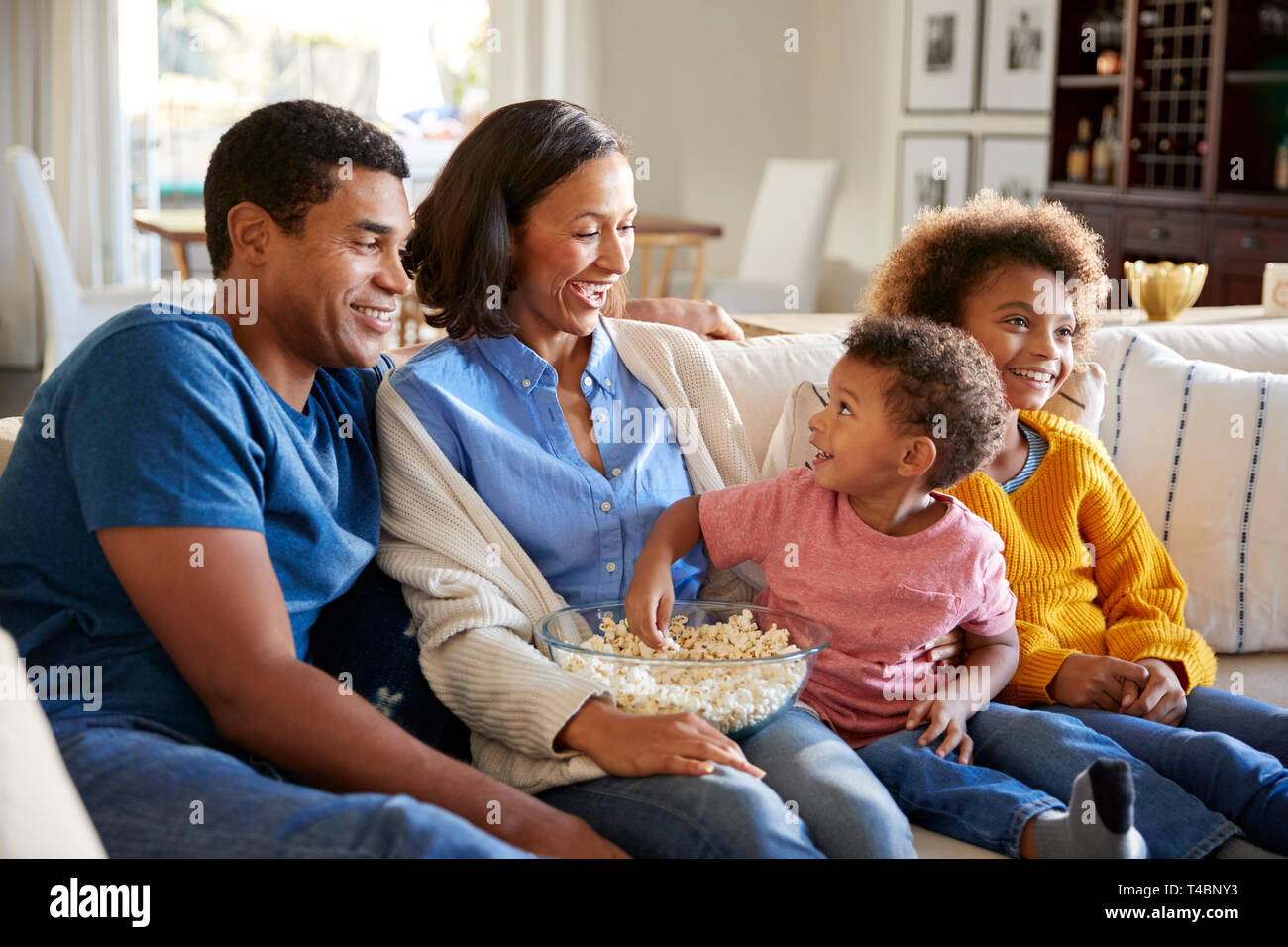Toddler boy eating popcorn, sitting on the sofa with his sister and parents in their living room watching a movie together Stock Photo